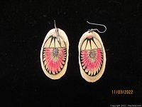 Front of oval-shaped cross cut earrings showing painted design with red and black feather or petal motif with central oval detail, metal hooks attached.