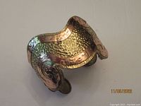 Angled photo showing hammered texture and copper scroll overlay with brass background on cuff bracelet.