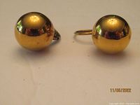 Front view of the pair of round dome-shaped gold tone earrings with reflective polished surfaces.