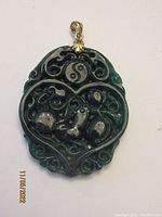 Front view of dark green jade pendant with intricate carvings, tonal variations and silver bail with leaf decoration.