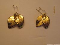 Pair of leaf shaped gold tone earrings with visible leaf vein design on a white background.