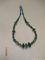 Full view of the 26-inch art glass necklace with a hook clasp, displaying multi-colored beads in blue, green, and purple shades.