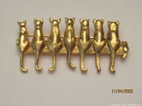 Front view of gold-tone metal brooch showing seven cat figures sitting in a row with curved tails.