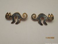 Pair of stylized black cat pins shown together, featuring geometric faces and curled tails.
