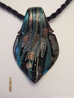 Front view of the Murano glass pendant showing metallic turquoise, silver, and gold colors with a leaf shape hung on a black rope.