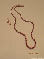 Full view of rhodonite bead necklace along with matching earrings laid flat on a surface.
