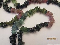 Close-up of the multi-color tourmaline tumble stones showing a range of colors including green, pink, and black in polished irregular shapes.