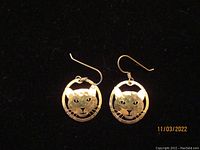 Pair of vintage circular cat face earrings with hooks shown on black background, metal with etched details
