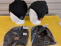 Two Bluetooth toques displayed on head mannequins, one floppy fleece-lined style with control panel and the other tight-fitting knit pattern style. Two additional toques inside plastic packaging shown in front.