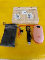Photo of two boxed rechargeable handwarmers, one USB cable, one wrist strap, and one black carrying pouch on a yellow background.