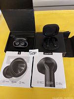 Two sets of true wireless earbuds in black, each with charging cases on top of their respective retail boxes in a yellow tray.