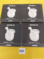 Photo shows 4 boxes of Aikela wireless earbuds in white with charging cases, model E12S, stacked in a 2x2 arrangement on a yellow surface.