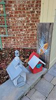 Two bird houses, one white resembling a church and one red with blue bird figure, plus wooden fish artwork board