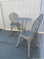 Full view of white metal bistro set on concrete patio showing table and two chairs with lattice design.