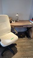 Office desk viewed with single center drawer, wood finish top and black metal legs. White office chair in front showing the wear on upholstery.