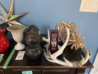 Overview of the collection showing faux antler, black metal candle holders, wooden heart decor, Galileo thermometer, and wooden starburst sculpture on a black table against a blue wall.
