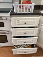 Four kitchen drawers partially open showing contents within including cutlery and kitchen linens in a plastic basket on the countertop.