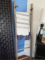 Wooden ladder leaning against blue and white wall with cream and blue throw blanket draped over the top rung next to a black lattice room divider and a black lamp on a small table.