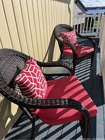 Two brown resin lawn chairs with red seat cushions and red/white geometric pillows on an outdoor balcony