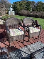 Two brown resin wicker arm chairs with cushions on red deck, front view