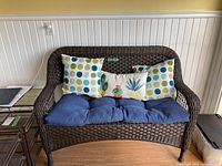 Full front view of brown wicker love seat with three decorative throw pillows and blue seat cushion.