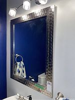 View of the full mirror mounted on bathroom wall with lighting and blue wall behind it.