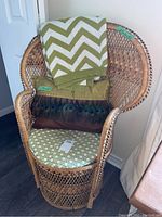 Rattan fan chair with green and white chevron blanket, green pillow, and peacock feather design pillow on seat.