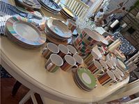 Wide view of the Royal Doulton Carnival pattern dishes laid out on a table showing plates, bowls, cups, mugs, and serving pieces.
