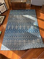 Top view of the full blue rug showing white patterned design on hardwood floor.