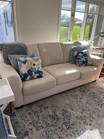 Front view of beige sofa with four throw pillows and grey blanket on left arm