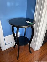 Side view of the black solid wood round table showing curved legs and circular lower shelf