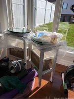 Two white wooden tables, each with woven basket insert. Tables are displayed next to a window with packing bubble wrap covering parts of the tables.