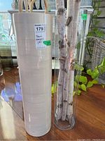 Photo showing both tall vases side by side with branches inside, placed on wooden floor next to a plant.