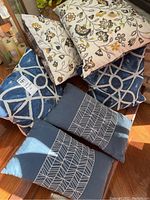 Six throw pillows arranged on floor showing floral and blue geometric patterns.
