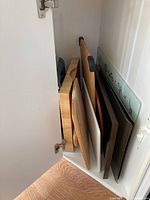 Cutting boards, trays, baking pans stored standing upright inside a white cabinet space