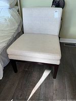 Front view of upholstered side chair showing cream colored fabric and dark wood legs.