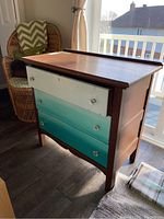 Front angle of the vintage three drawer dresser with painted drawers showing gradient blue color and glass pulls.