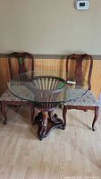 Full view of antique wood pedestal table with round glass top and two matching wooden chairs with upholstered seats; shows overall structure and finish.