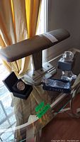 Metal antique desk lamp with four smaller items on glass table including crystal pieces, clock box, and Oleg Cassini votive