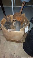 Box filled with multiple cast iron and metal pots and pans showing rust and scratches.