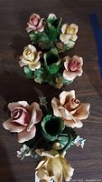 Three Capodimonte floral ceramic candle holders featuring rose designs and green leaf bases, photographed from an overhead angle on a wooden surface.