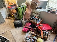 Wide view of green suitcase, mannequin torso, crockpot case, wicker basket, assorted items on floor