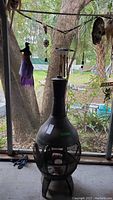 Full front view of tall black metal fire pit with mesh sides and chimney top near window.