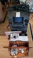 GPX karaoke machine with microphone placed on top, wooden towel holder and boxed fan in front.