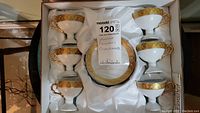 Full set of 6 ceramic pedestal cups with matching saucers inside the box with white satin lining. The cups and saucers have gold trim details.