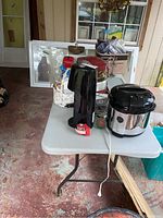Full view of items on table including SodaStream, rice cooker, tape dispenser, metal cooling rack, white container, and fold-up table.