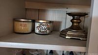 Two scented candles and an ornate metal candle holder on a shelf