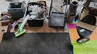 Overview photo showing various items including a plastic storage bin filled with miscellaneous items, mop, metal dog crate, diaper genie, wire shelving, and wire decorations.