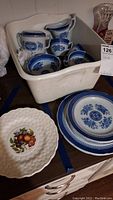 Several blue and white Spode dishes including sugar bowl, creamer, cups, bowls, and matching plates. Also present is a white plate with a fruit decal.