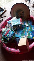 Top view of pink inflatable kiddie pool filled with boxed pool floats, goggles, and other pool accessories, showing weathered condition and dirt.